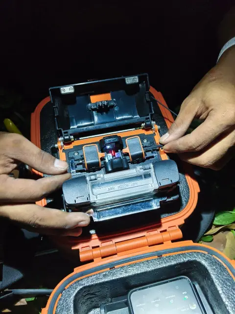 Penyambungan kabel fiber optik dengan mesin splicer di lapangan pada malam hari